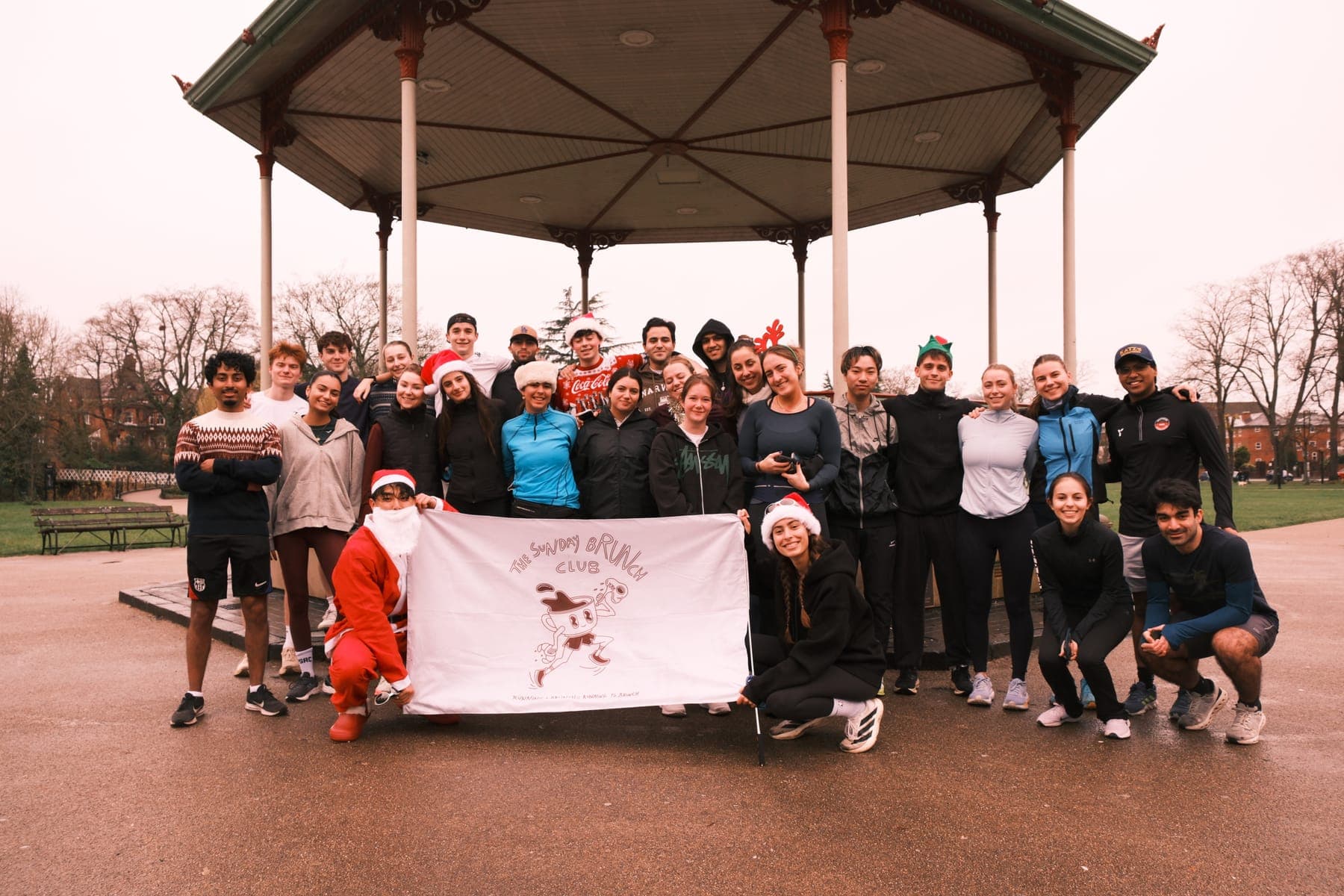Sunday Brunch Club runners in santa hats holding the club banner at the bandstand
