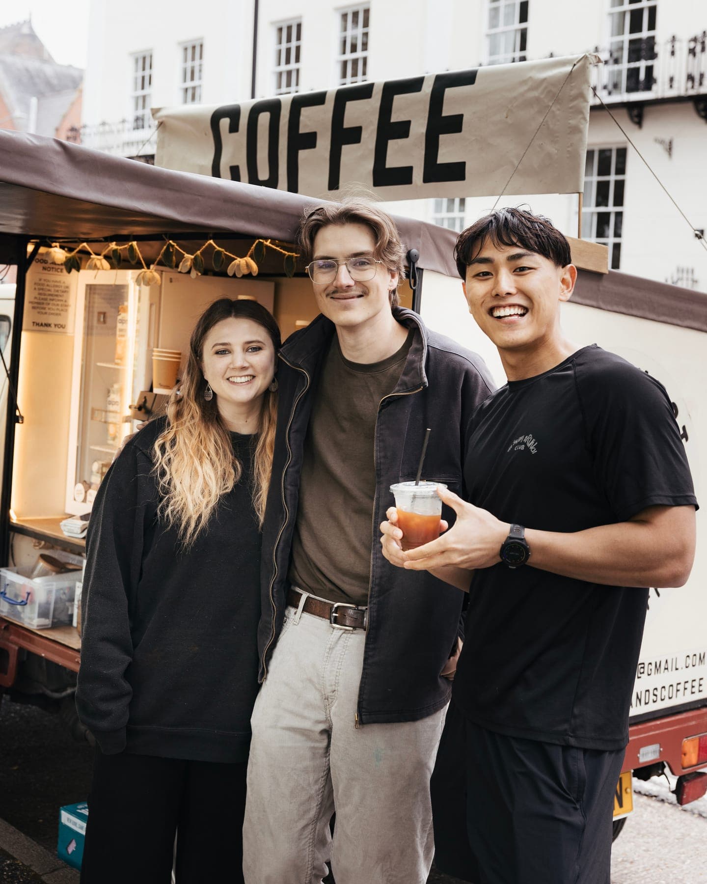 A runner holding an iced coffee with two people from a coffee van
