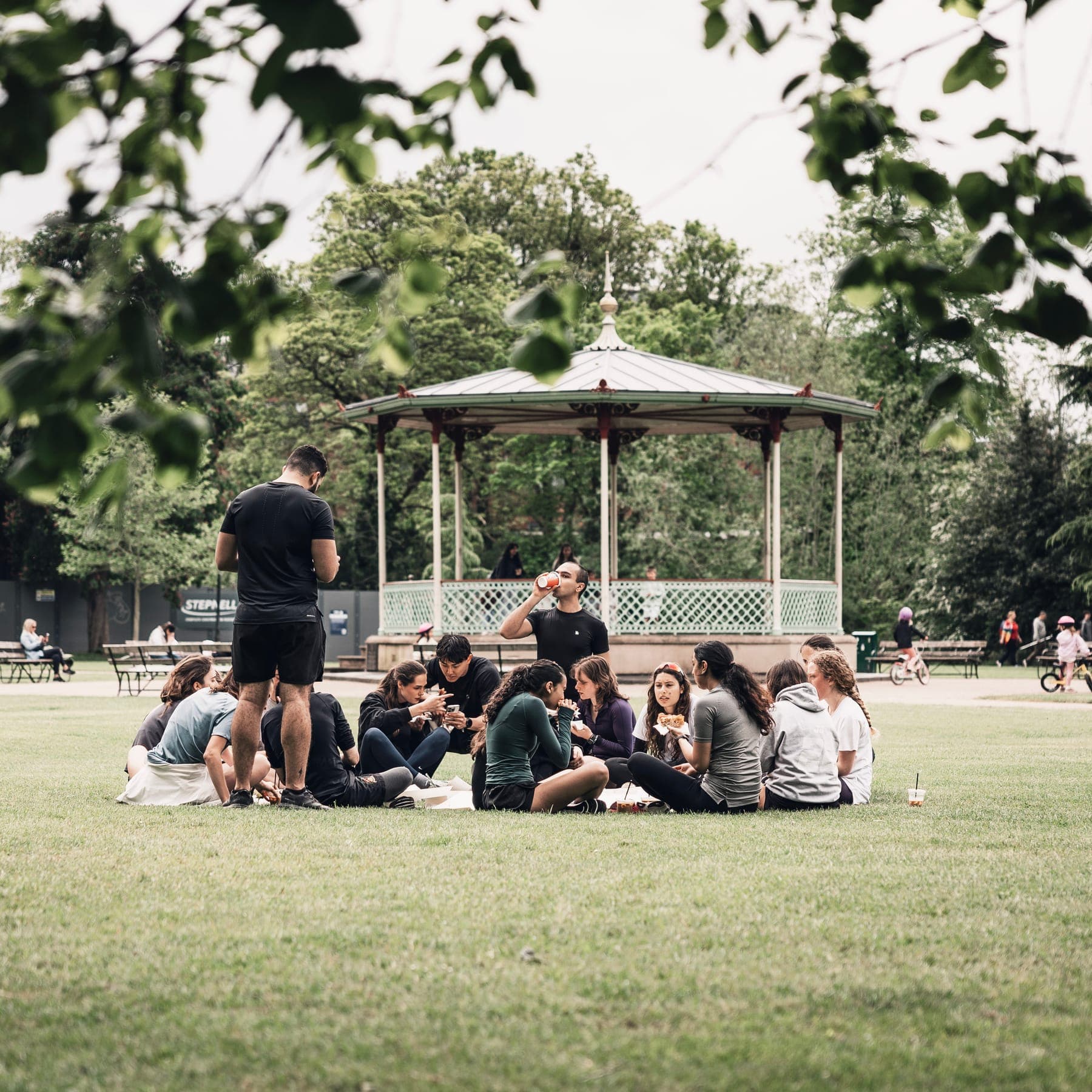 Runners sitting in a circle on the grass by the bandstand with coffees and pastries